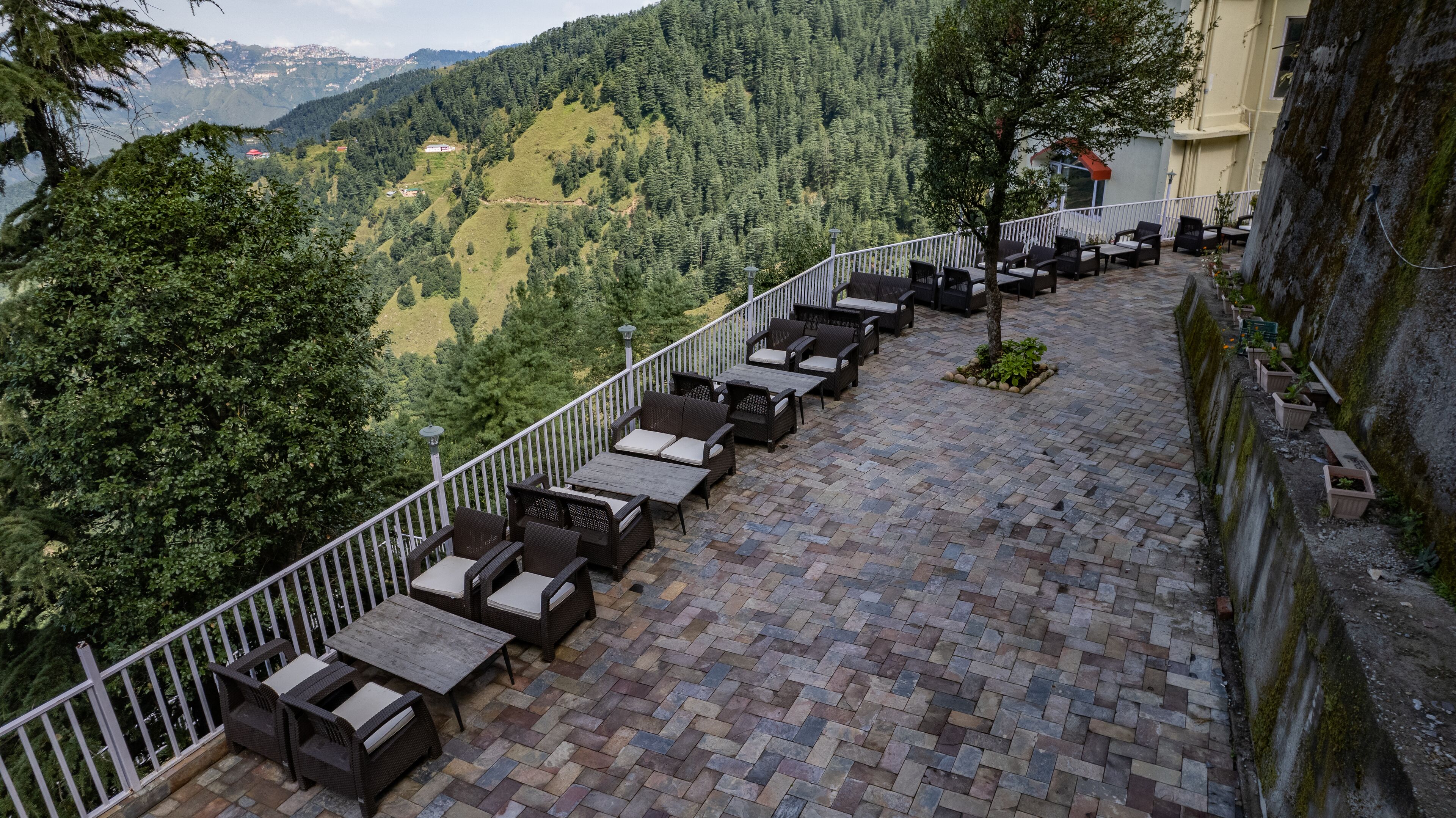 A terrace with wicker furniture and a stone floor, overlooking a mountainous landscape.