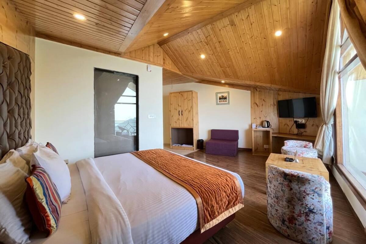 A bedroom with a large bed, a sofa, a TV, and a wooden ceiling.