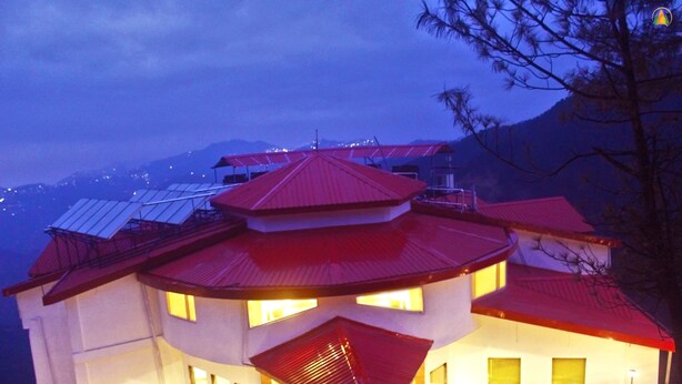Un edificio de varios pisos con techo rojo, múltiples ventanas y paneles solares en el techo.