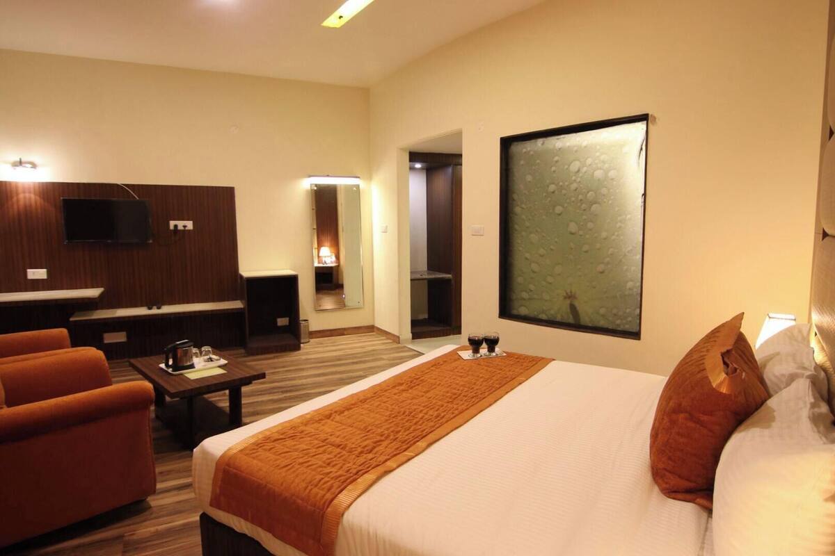 A hotel room with a bed, two armchairs, a coffee table, a TV, and a large window.