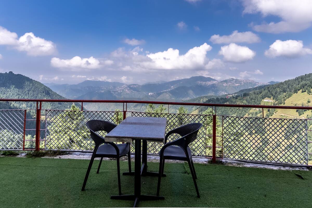 A terrace with a table and chairs, overlooking a mountainous landscape.