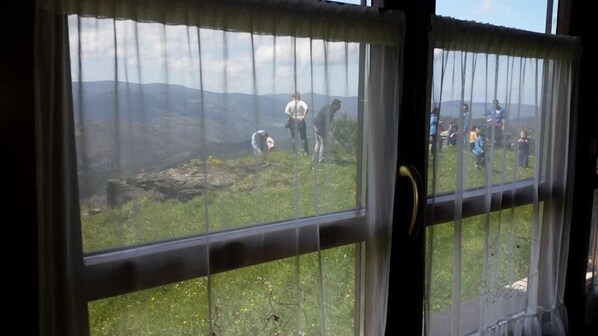 Visão pela janela com um campo gramado e montanhas ao longe.