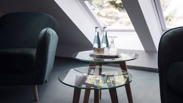 Una habitación moderna con una mesa de vidrio, dos sillas verdes y un ventanal con vistas a árboles.