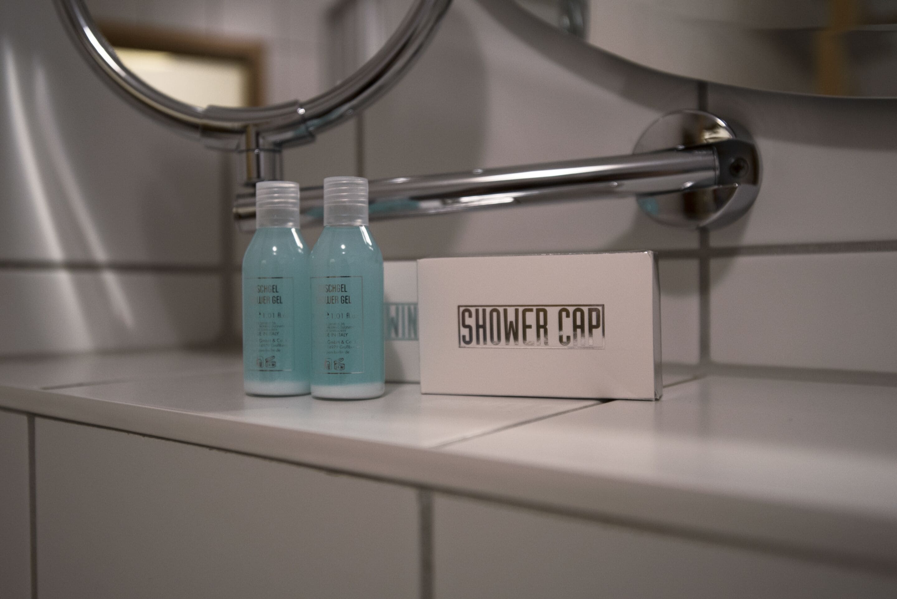 A bathroom with a shower cap and two bottles of shower gel on a counter.