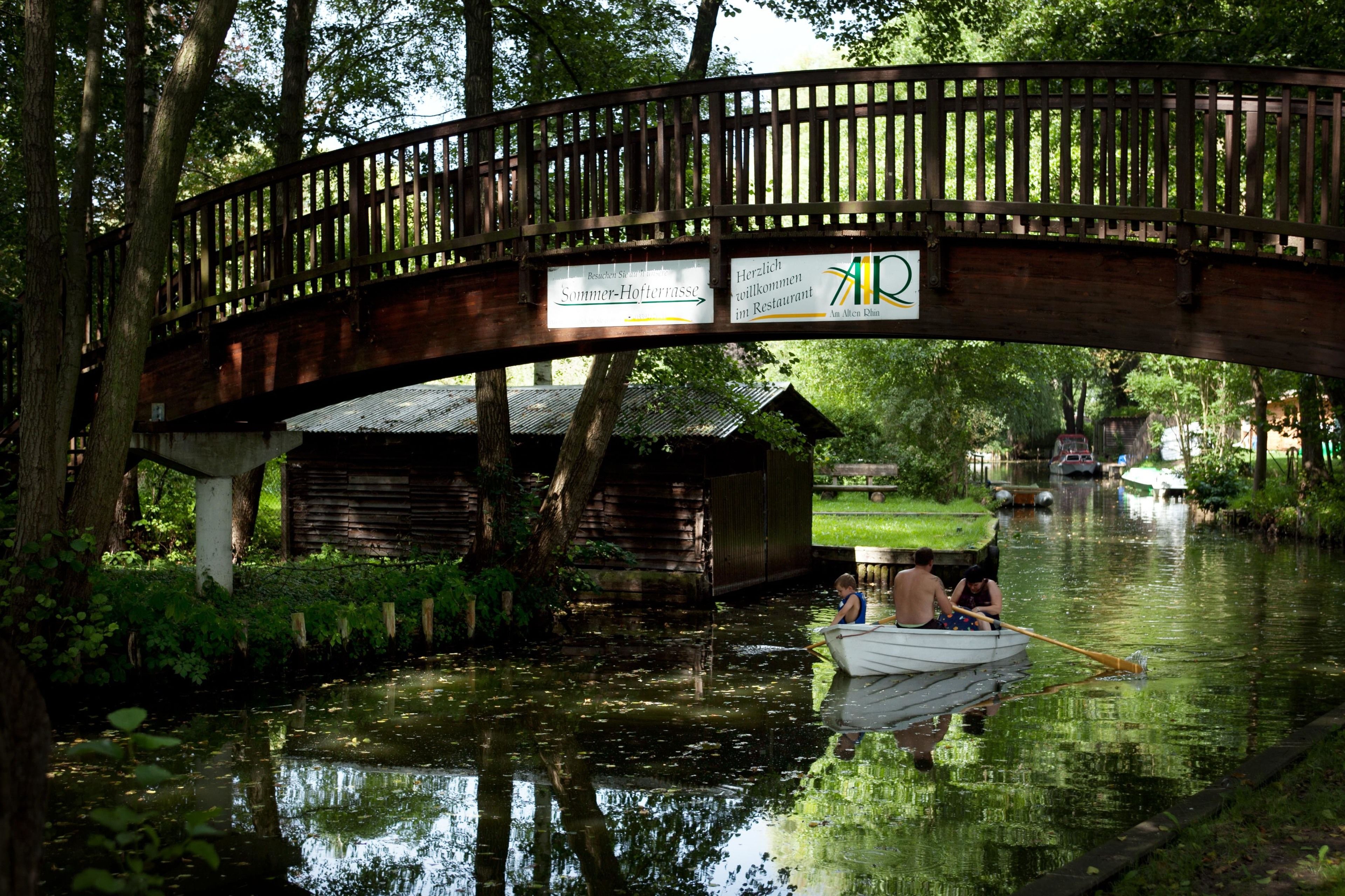 Un puente de madera sobre un río tranquilo, con una barca y gente.