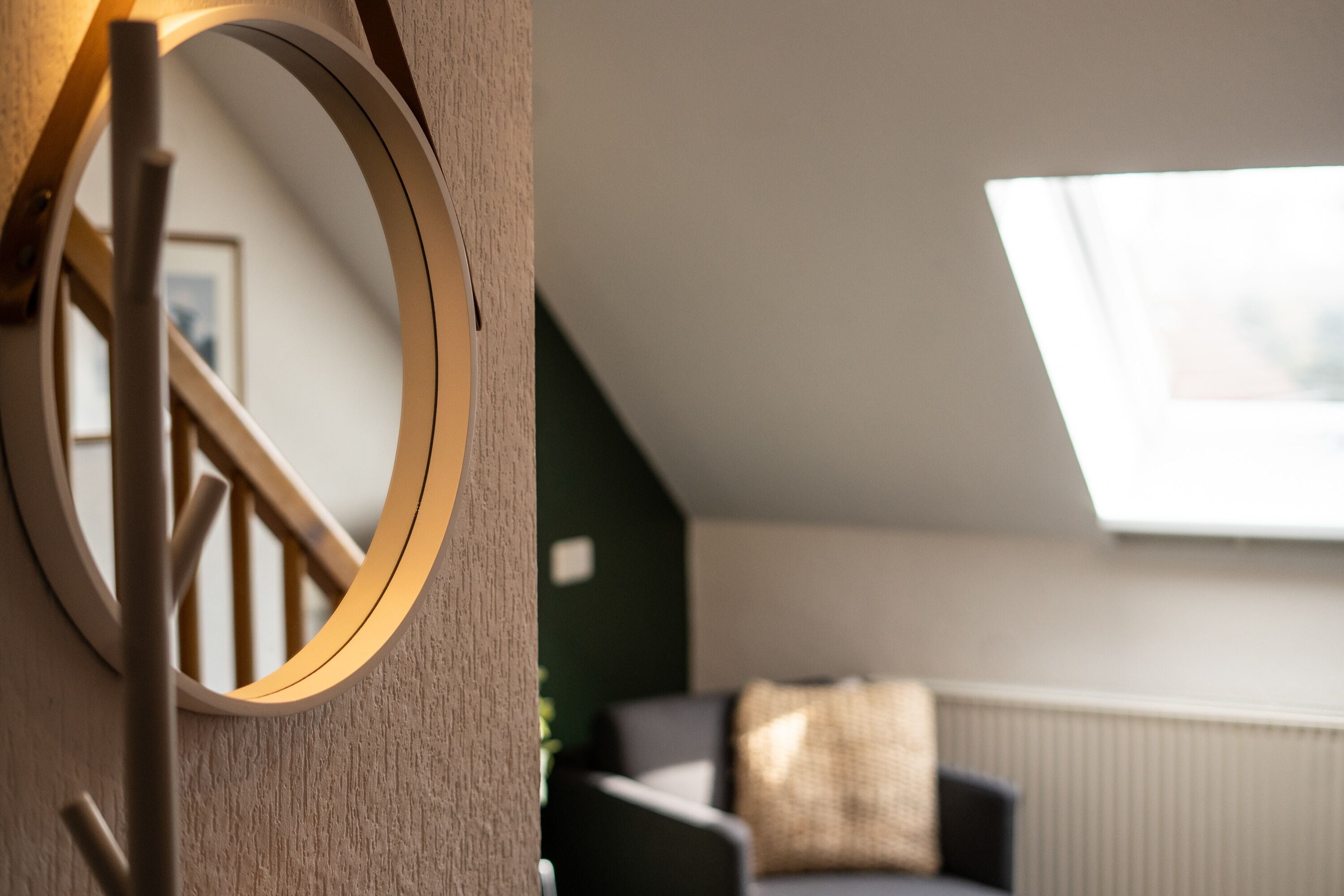 A modern interior with a wooden staircase, a round mirror, a dark-colored sofa, and a skylight.