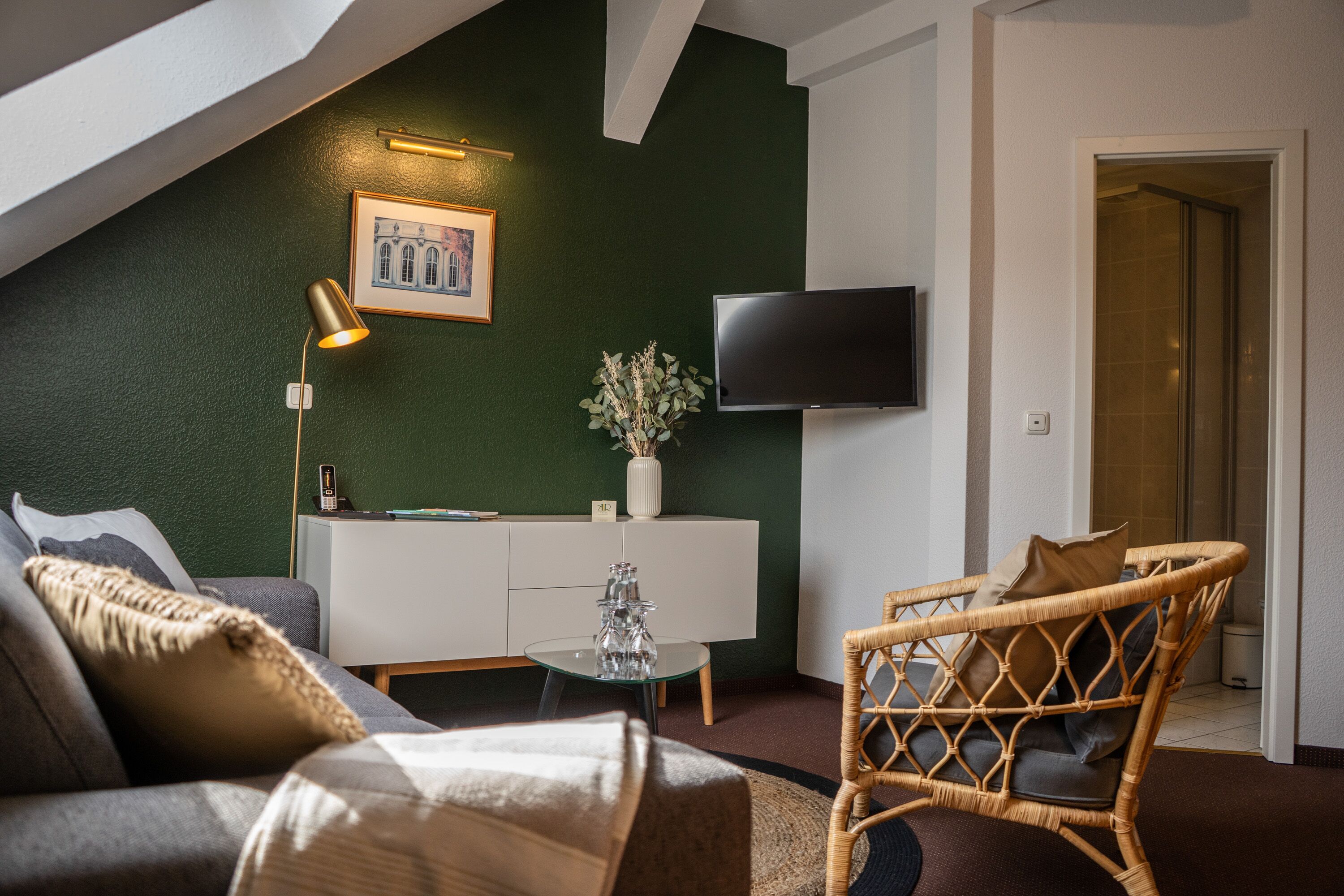 Una sala de estar moderna con una pared verde decorativa, un televisor de pantalla plana, un sofá, una mesa de centro y una silla de mimbre.