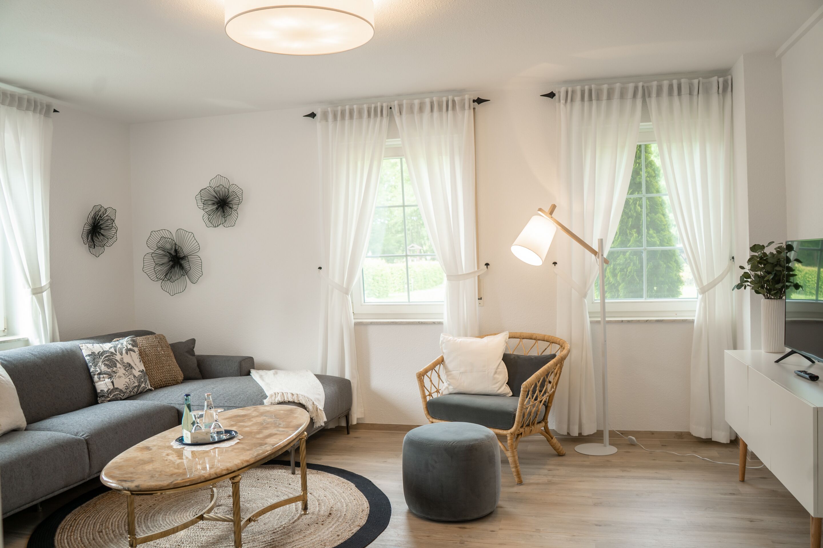 A modern living room with a sofa, ottoman, and coffee table, a wicker chair, a floor lamp, and decorative wall art.