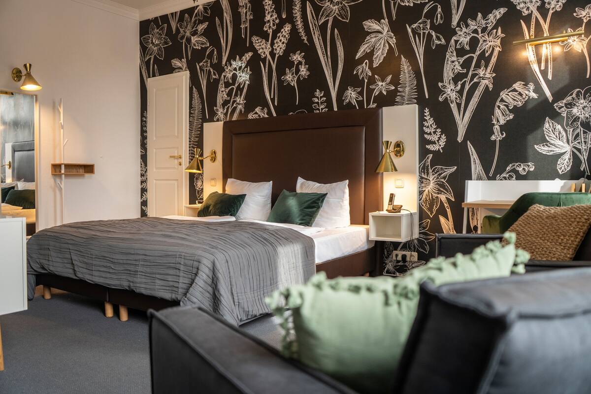 Quarto com uma cama grande, mesa de cabeceira e parede com papel de parede floral.