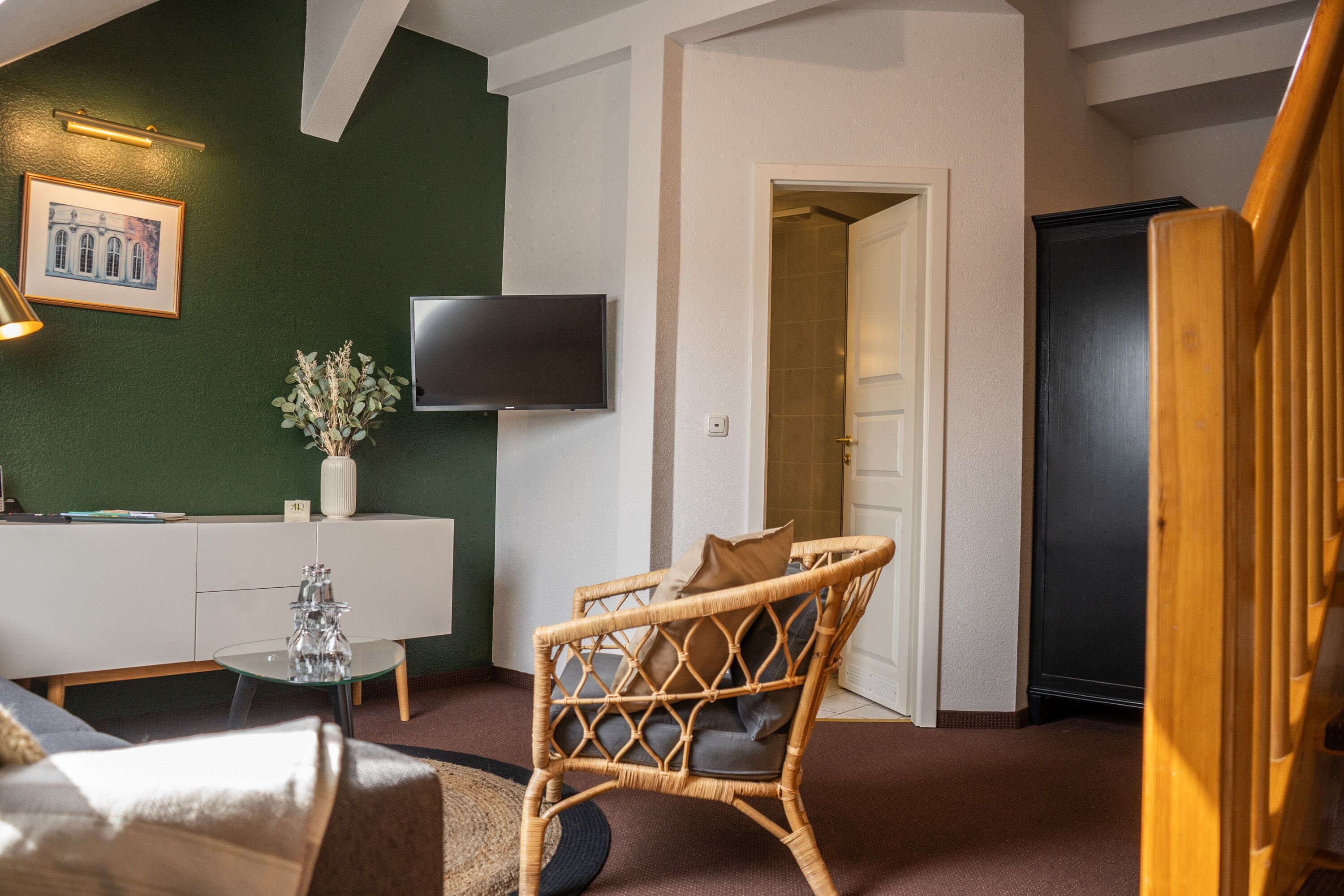 A modern living room with a green accent wall, a flat-screen TV, a wicker chair, and a white console table.