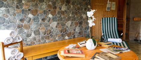 A stone wall, wooden furniture, a bench, a chair, and a small table with books and a vase of flowers.