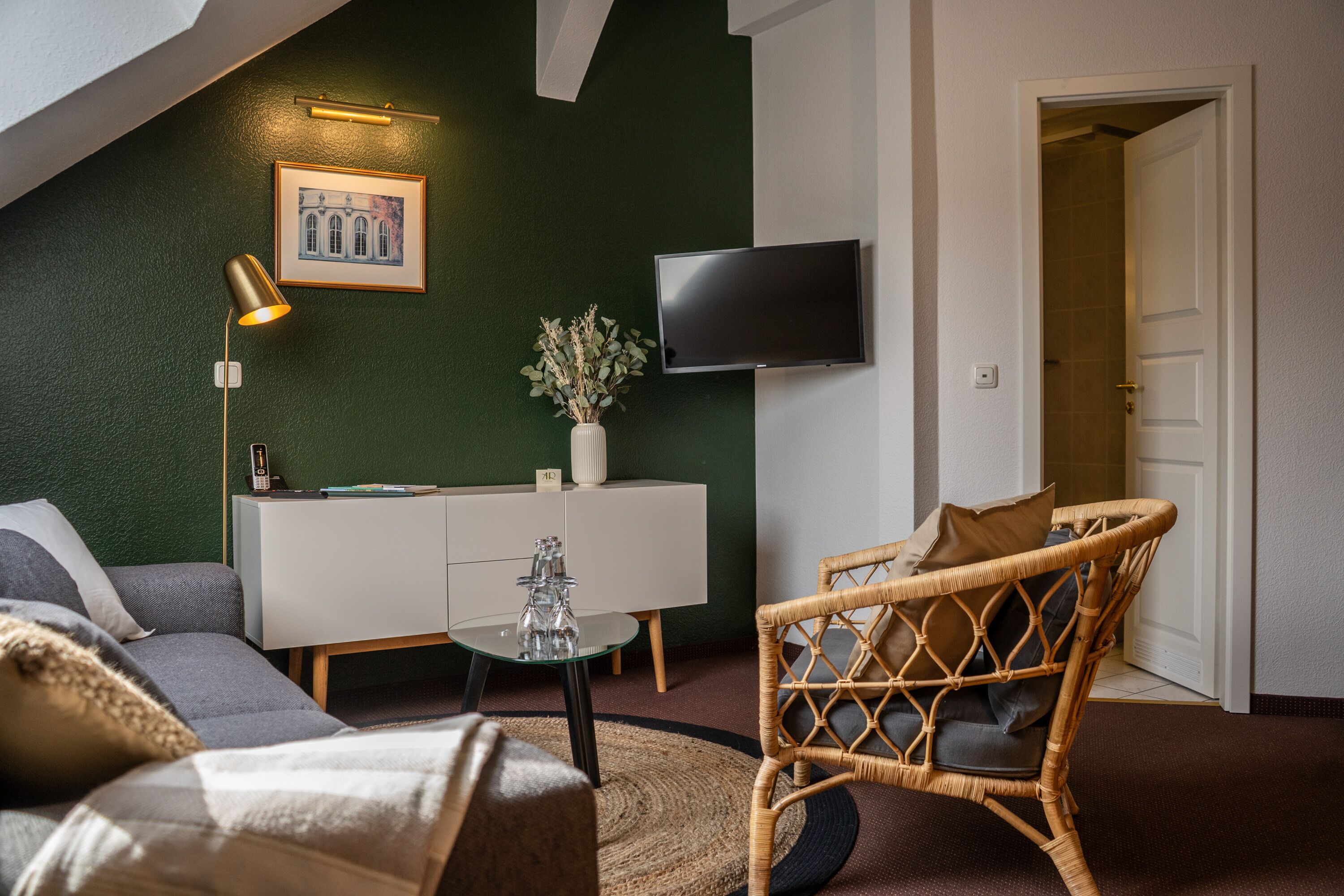 Una sala de estar moderna con una pared de acento verde, un televisor de pantalla plana, una silla de mimbre, un sofá y una mesa de centro de vidrio.