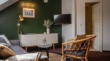 Un salon moderne avec un mur d’accent vert, un téléviseur à écran plat, un fauteuil en osier, un canapé et une table basse en verre.