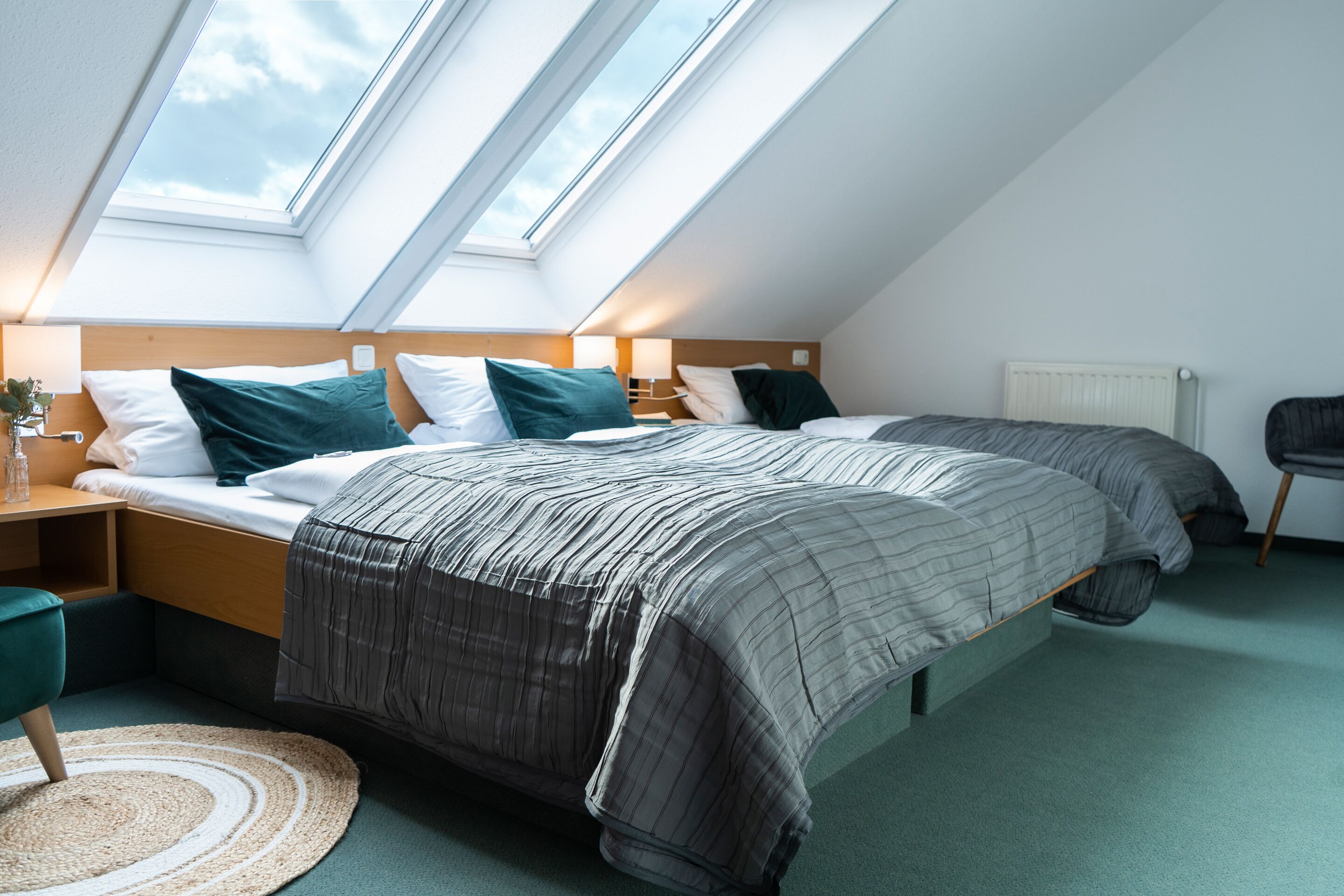 A modern bedroom with two beds, skylights, a round rug, and a radiator.