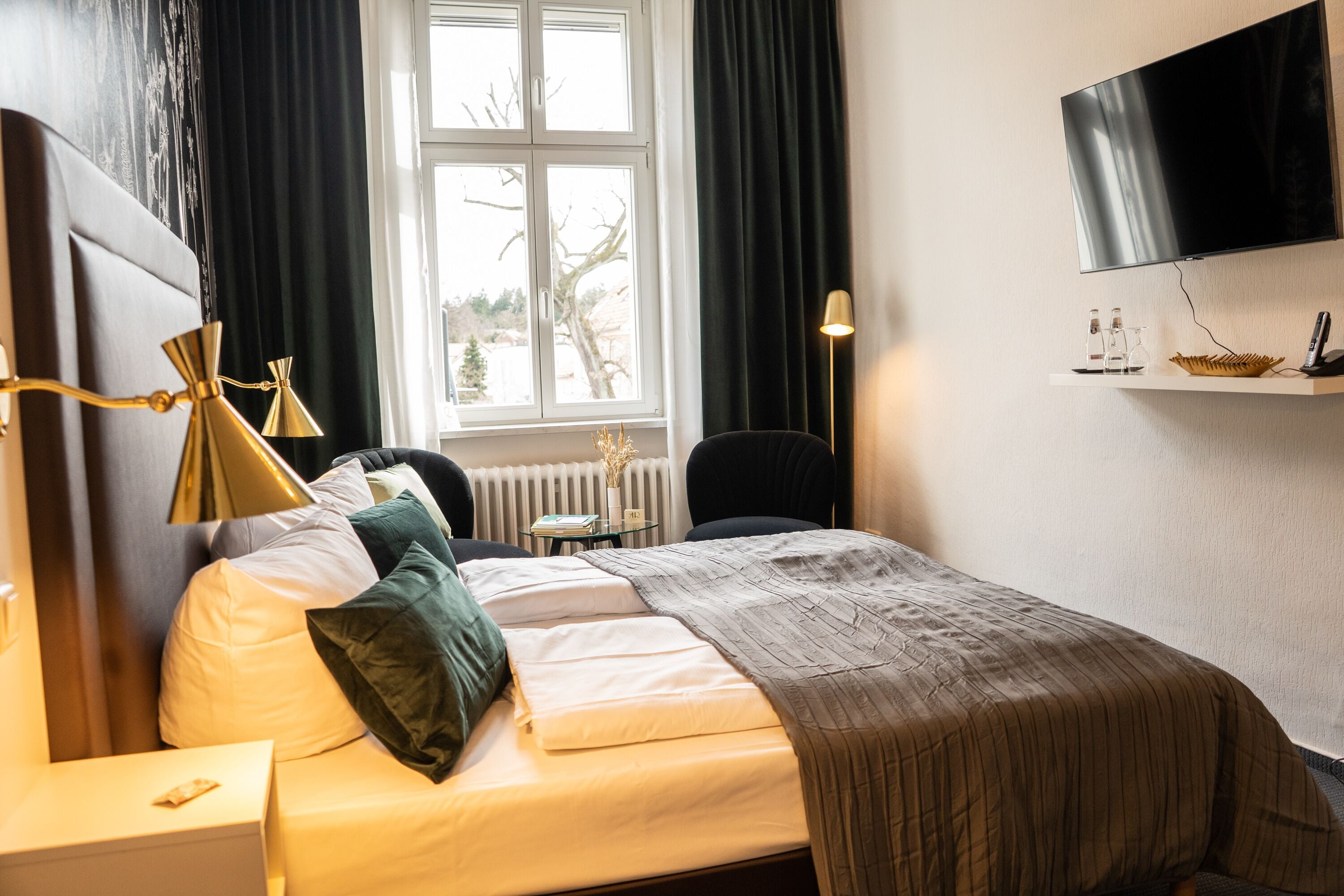 A neatly arranged hotel room with a bed, bedside table, lamp, and a mounted TV.