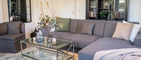 A living room with a sectional sofa, a glass coffee table, a bookshelf, and a mirror.