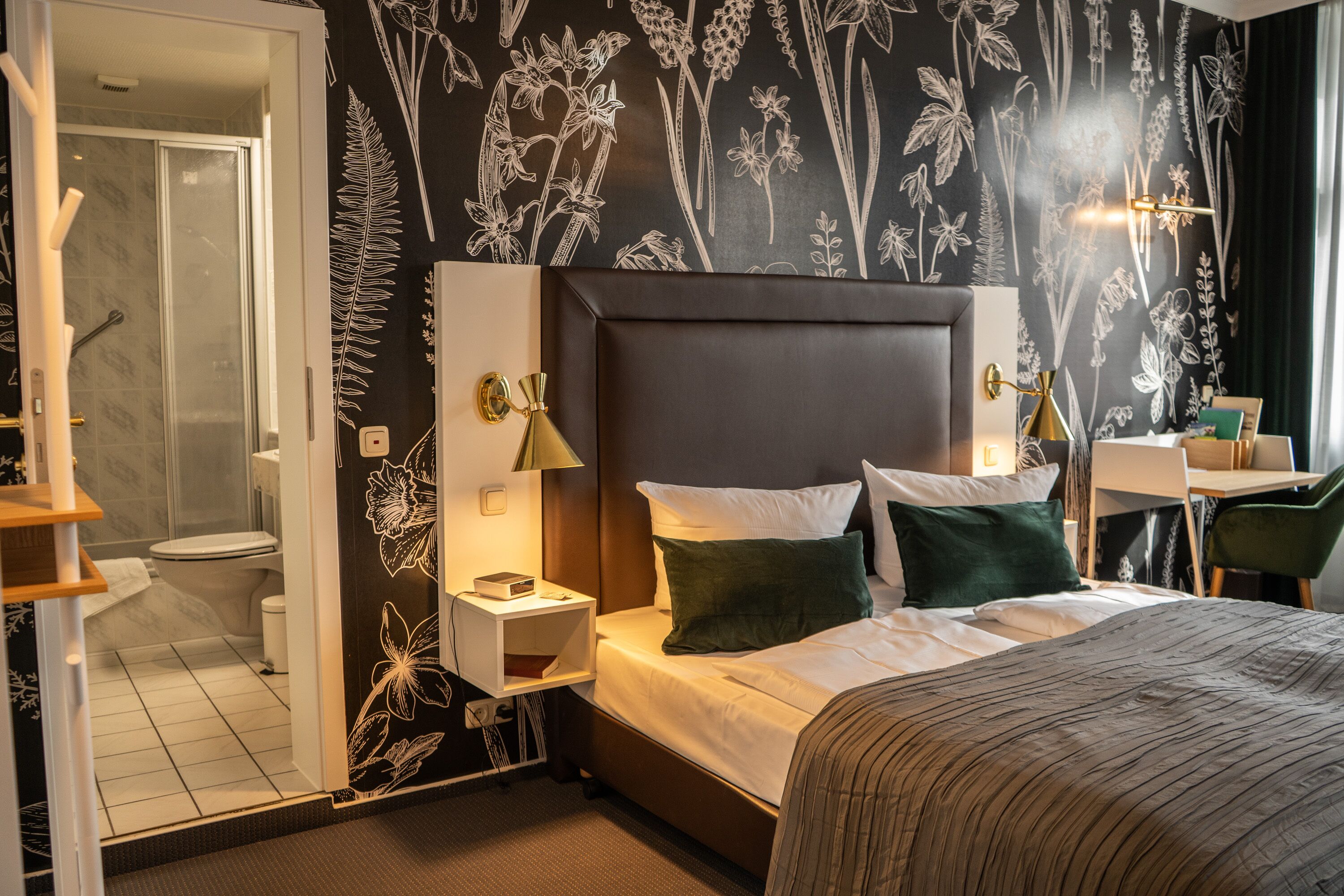 A hotel room with a bed, bedside tables, a desk, and a shower area.