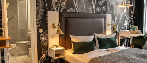 A hotel room with a bed, bedside tables, a desk, and a shower area.