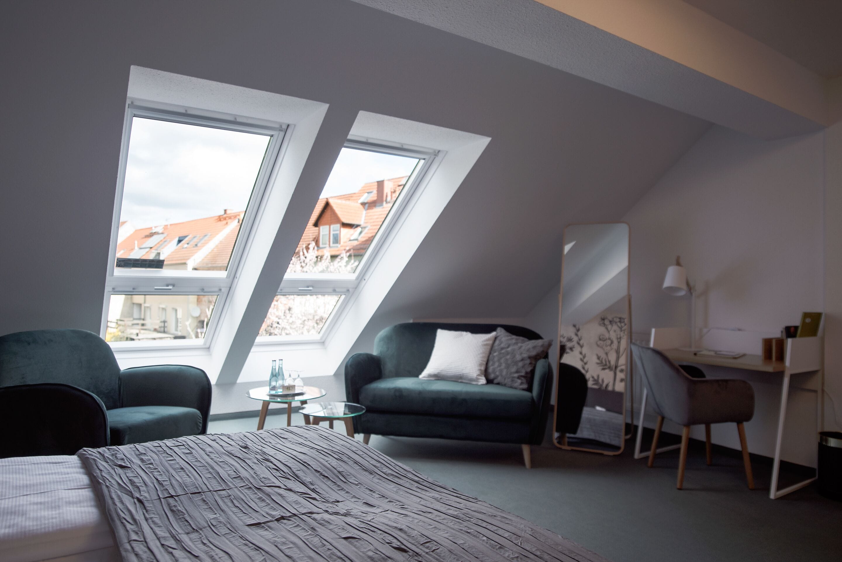 A modern loft bedroom with a sloped ceiling, two skylights, a bed, a desk, and a sofa.