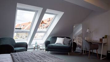 A modern loft bedroom with a sloped ceiling, two skylights, a bed, a desk, and a sofa.