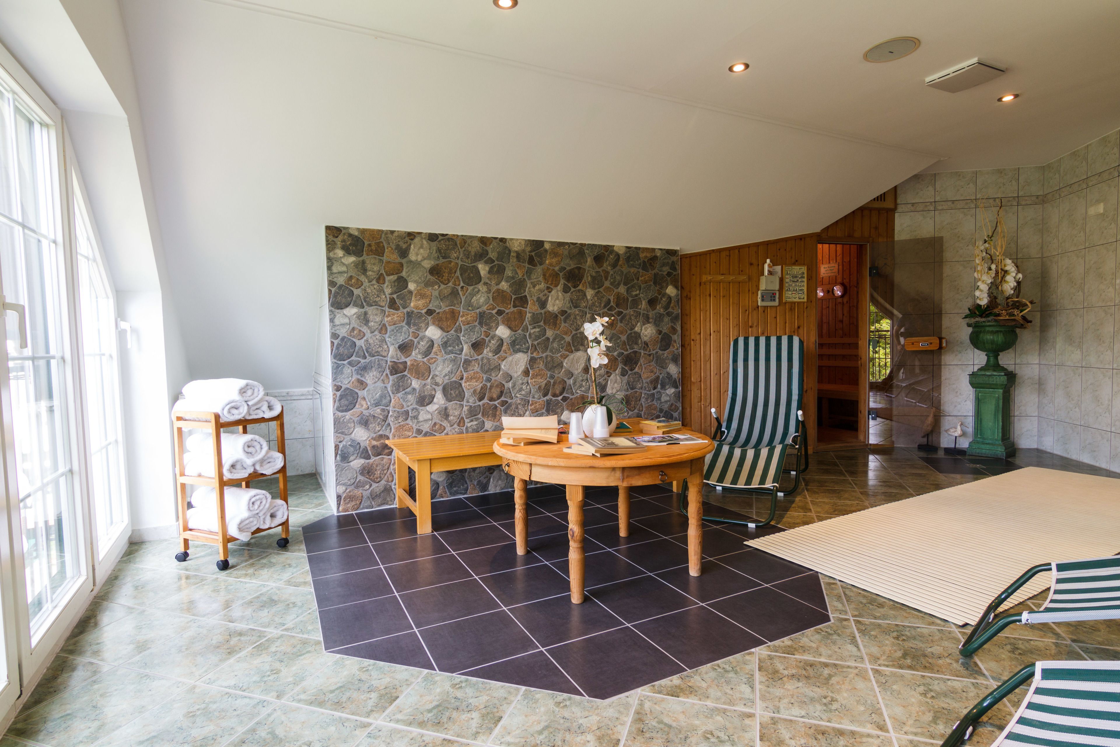 A spacious room with a stone wall, a wooden table with chairs, a bench, and a rack of towels.