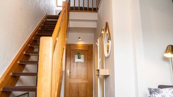 A wooden staircase leading to a door with a small window, a wall-mounted mirror, and a lamp.
