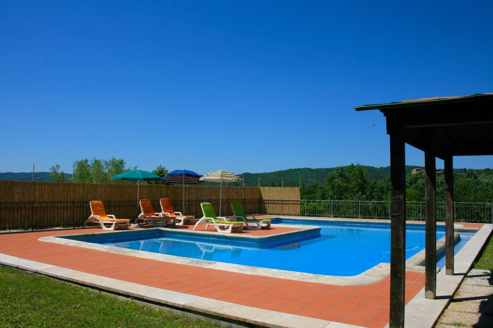 Una piscina rectangular con cubierta de madera, rodeada de sillas de descanso y sombrillas.
