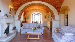 A cozy living room with a fireplace, floral sofas, and a brick ceiling. - Stunning private villa for 8 guests with private pool, WIFI, TV, terrace, pets allowed and parking (Lucignano)