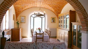 A dining area with a brick arch, a chandelier, a table set for four, and a cabinet with glass doors. - Stunning private villa for 8 guests with private pool, WIFI, TV, terrace, pets allowed and parking (Lucignano)