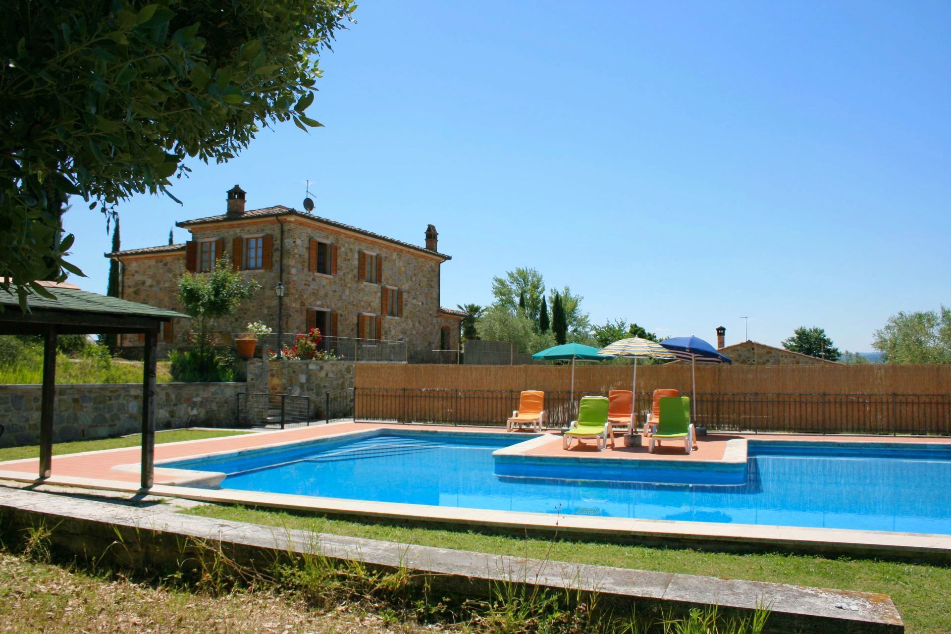 A swimming pool with lounge chairs and umbrellas, surrounded by a stone building and greenery.