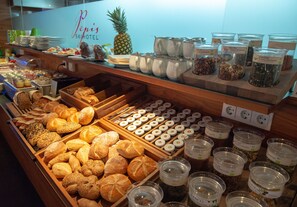 A breakfast buffet with various breads, pastries, and condiments.
