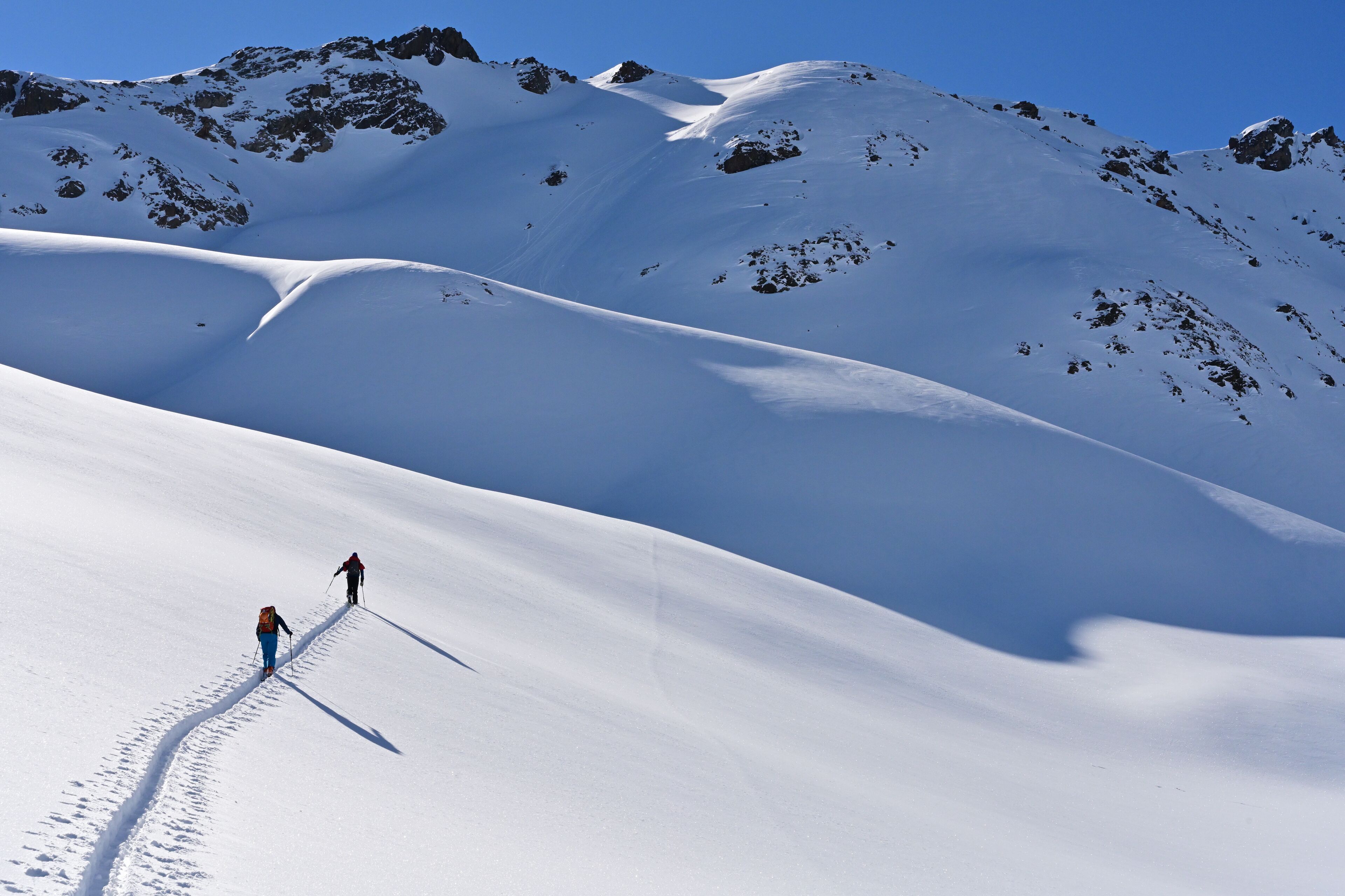 Paisaje nevado de montaña con dos personas caminando.