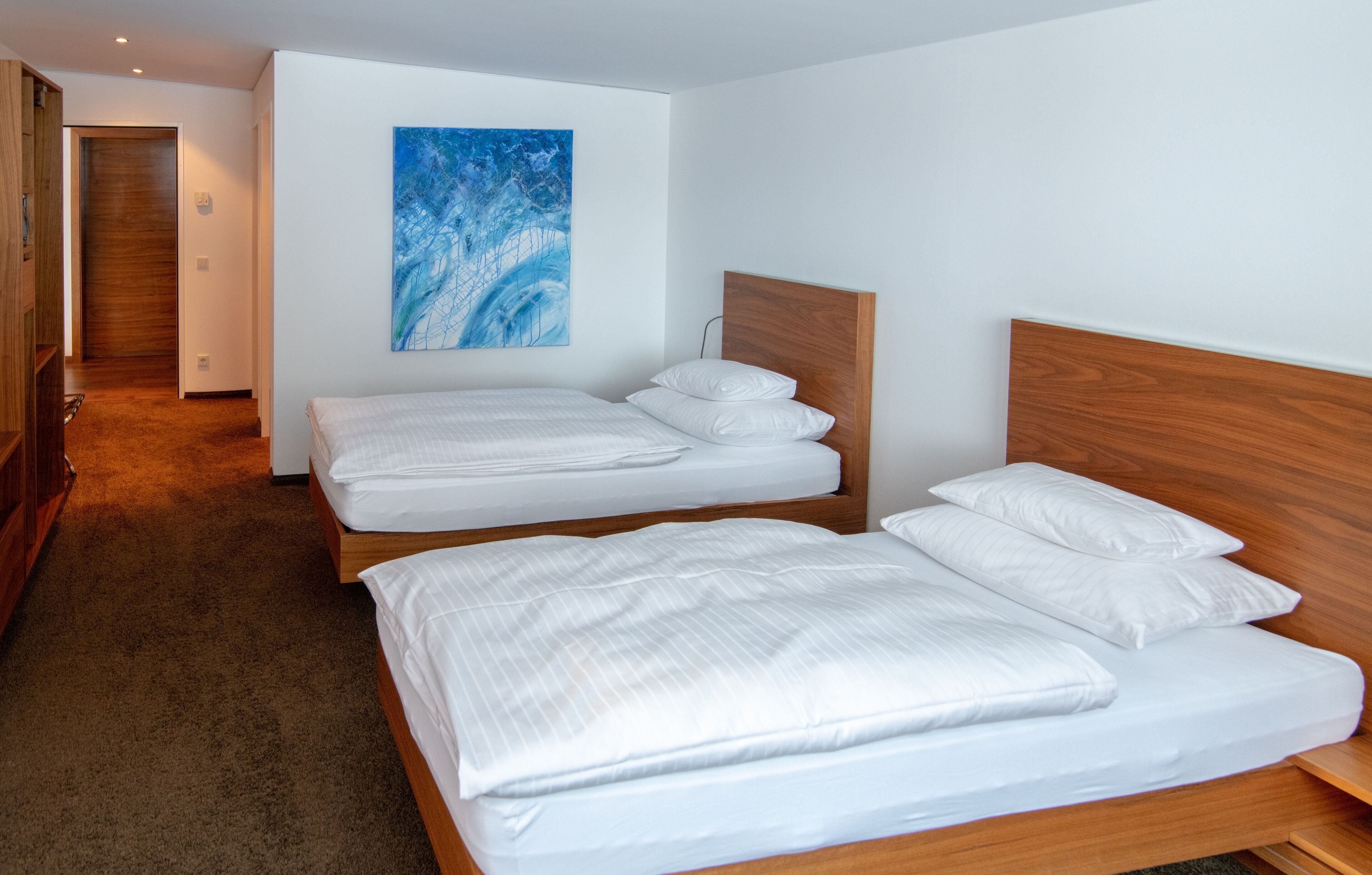 A hotel room with two beds, a wooden headboard, a large abstract painting, and a carpeted floor.