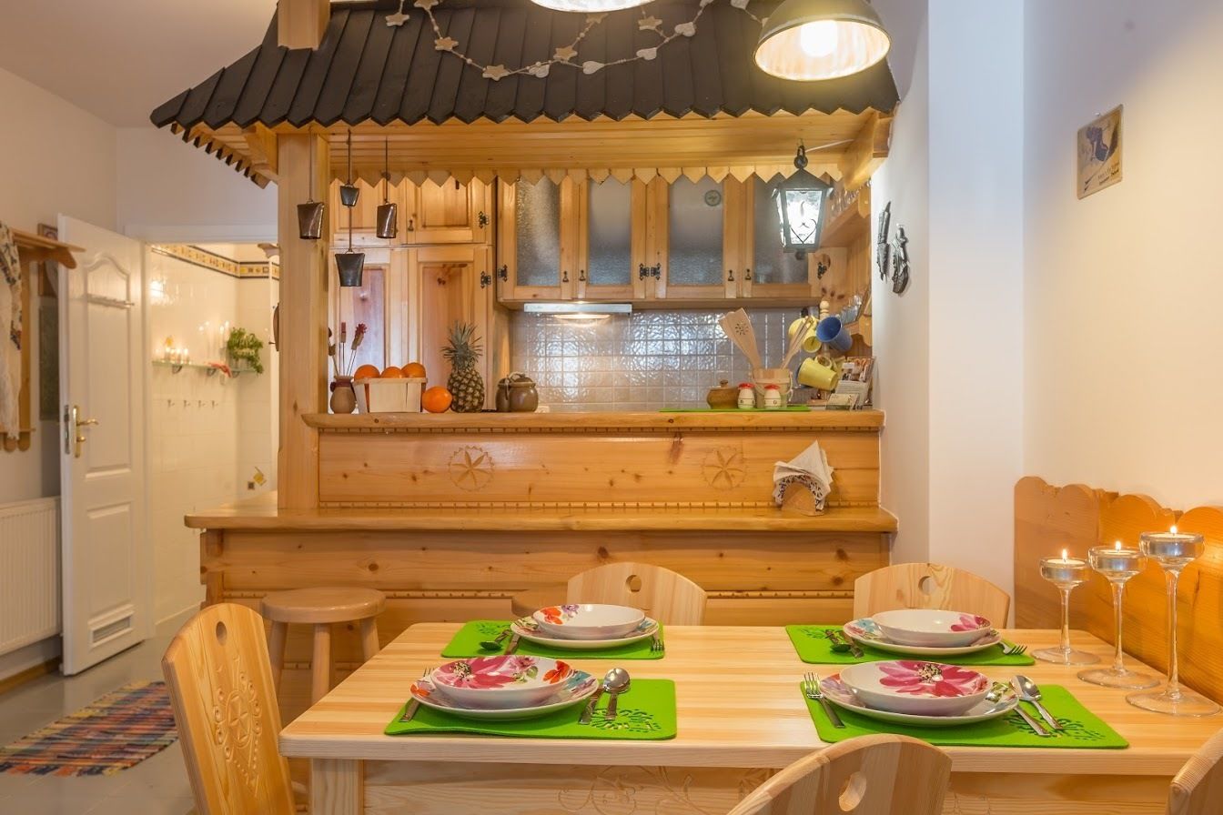 A wooden dining area with a high wooden counter, a table set for four with plates, cutlery, and glasses, and a small kitchen area with a refrigerator and various kitchen items.