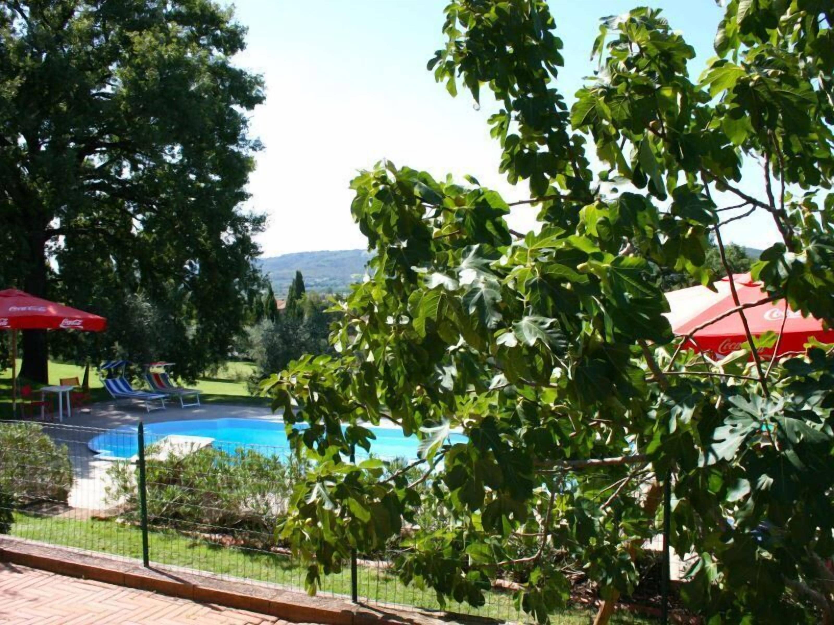 Zona de piscina con piscina cercada, sombrillas rojas y vistas del paisaje circundante.