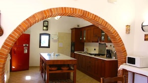 Una cocina con un arco de ladrillo, armarios de madera, un refrigerador rojo, un microondas blanco y una mesa con tazones.