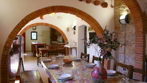 Un comedor con una mesa larga dispuesta para seis personas, bajo un arco de ladrillo. Hay macetas colgando en la pared sobre la mesa.