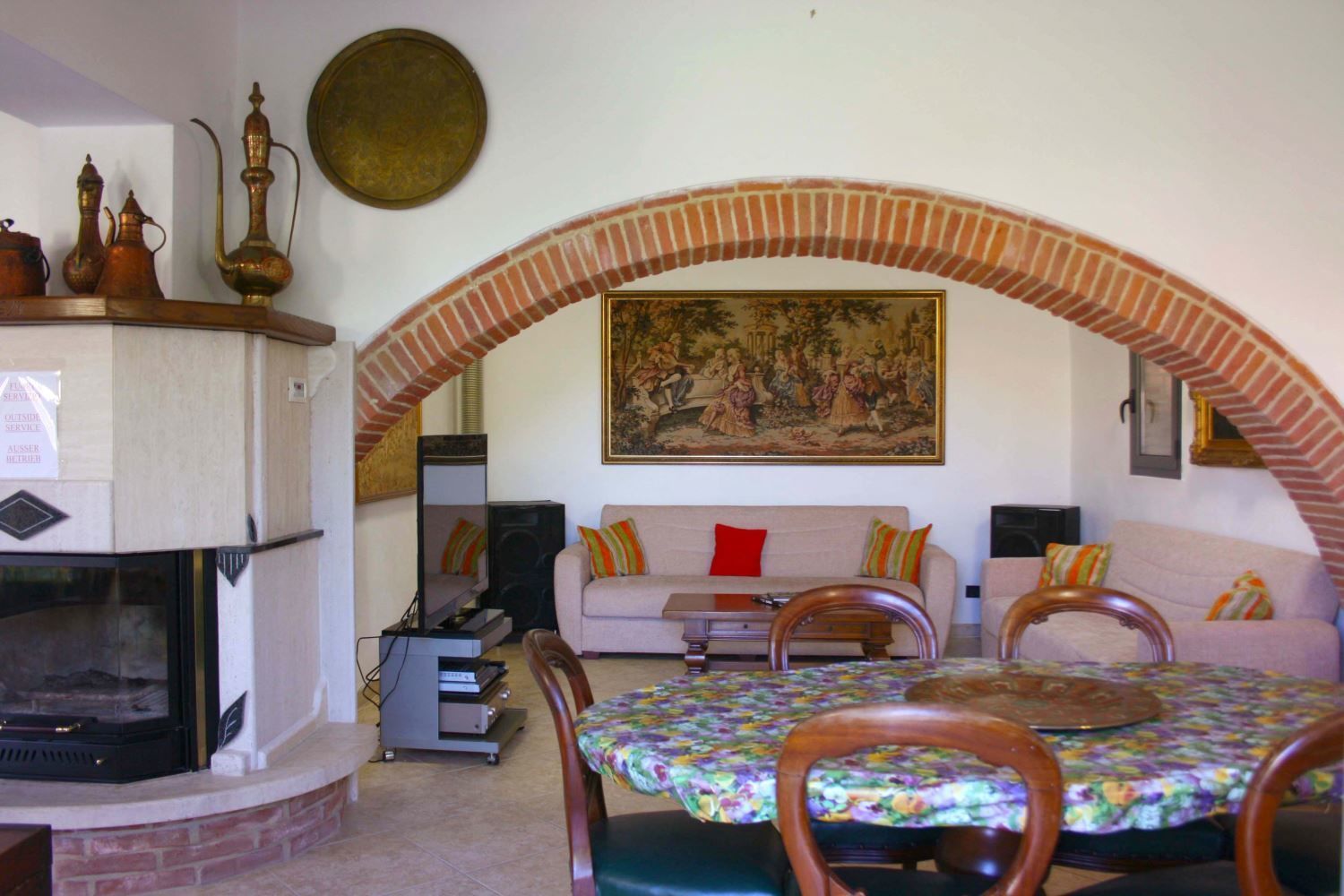 A living room with a fireplace, a sofa set, a dining table with chairs, and a large painting on the wall.