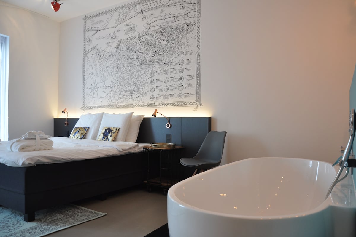 Moderni hotellihuone, jossa on suuri sänky, seinällä kartta, kylpyamme ja työpöytä tuolilla.