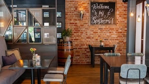 Un cafè acollidor amb una paret de maó, un cartell de benvinguda i diferents opcions de seients, com ara un sofà, taules i cadires.