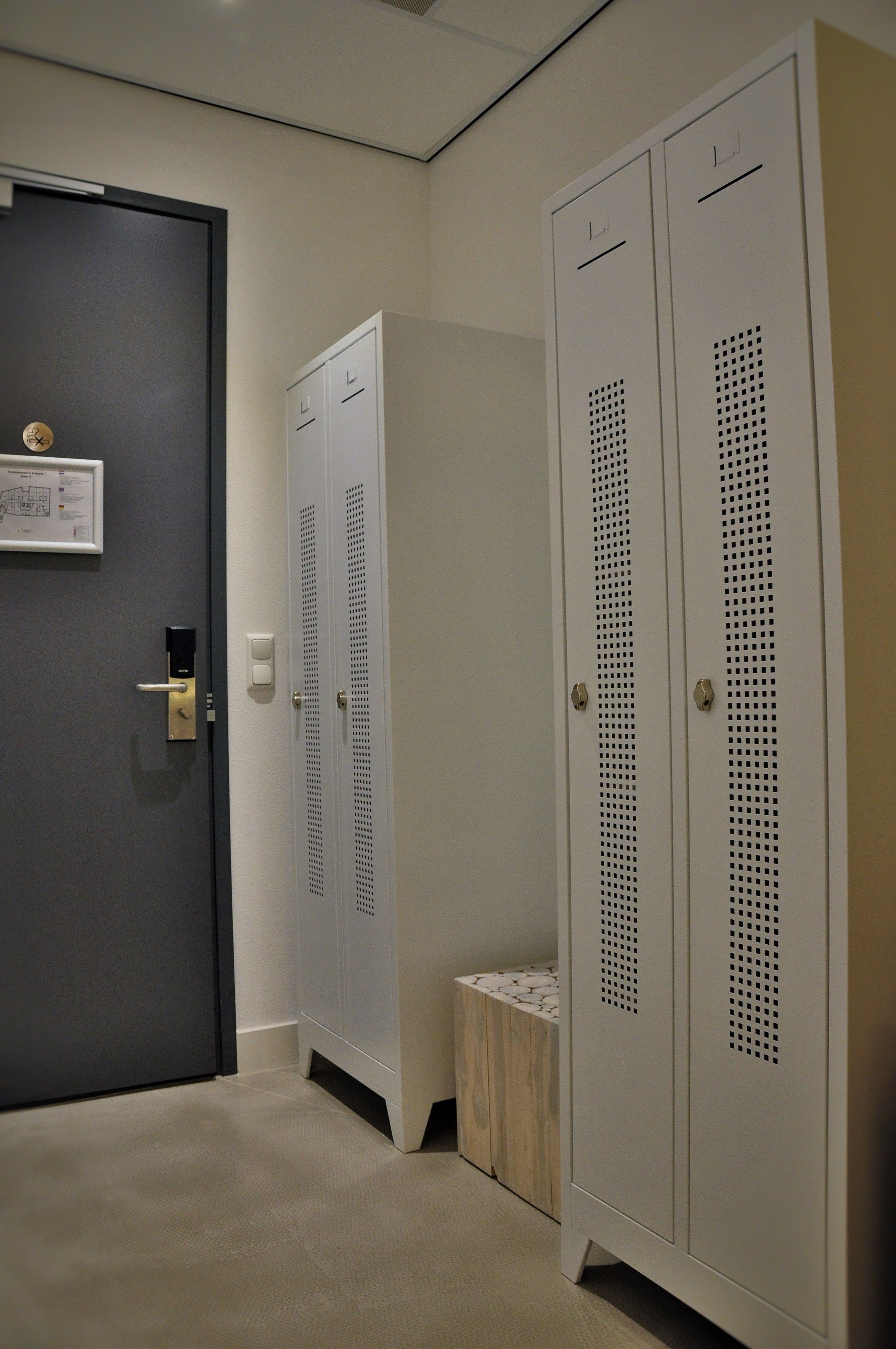 A hallway with a dark door, a light switch, and a small wooden bench.