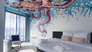 Una habitació d'hotel moderna amb un llit gran, una zona d'estar i un mural al sostre.