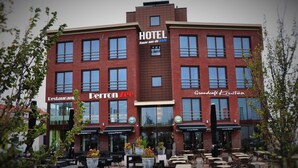 Un hotel amb façana de maó vermell, diversos rèstols de senyals, terrasses exteriors i un cel serè.