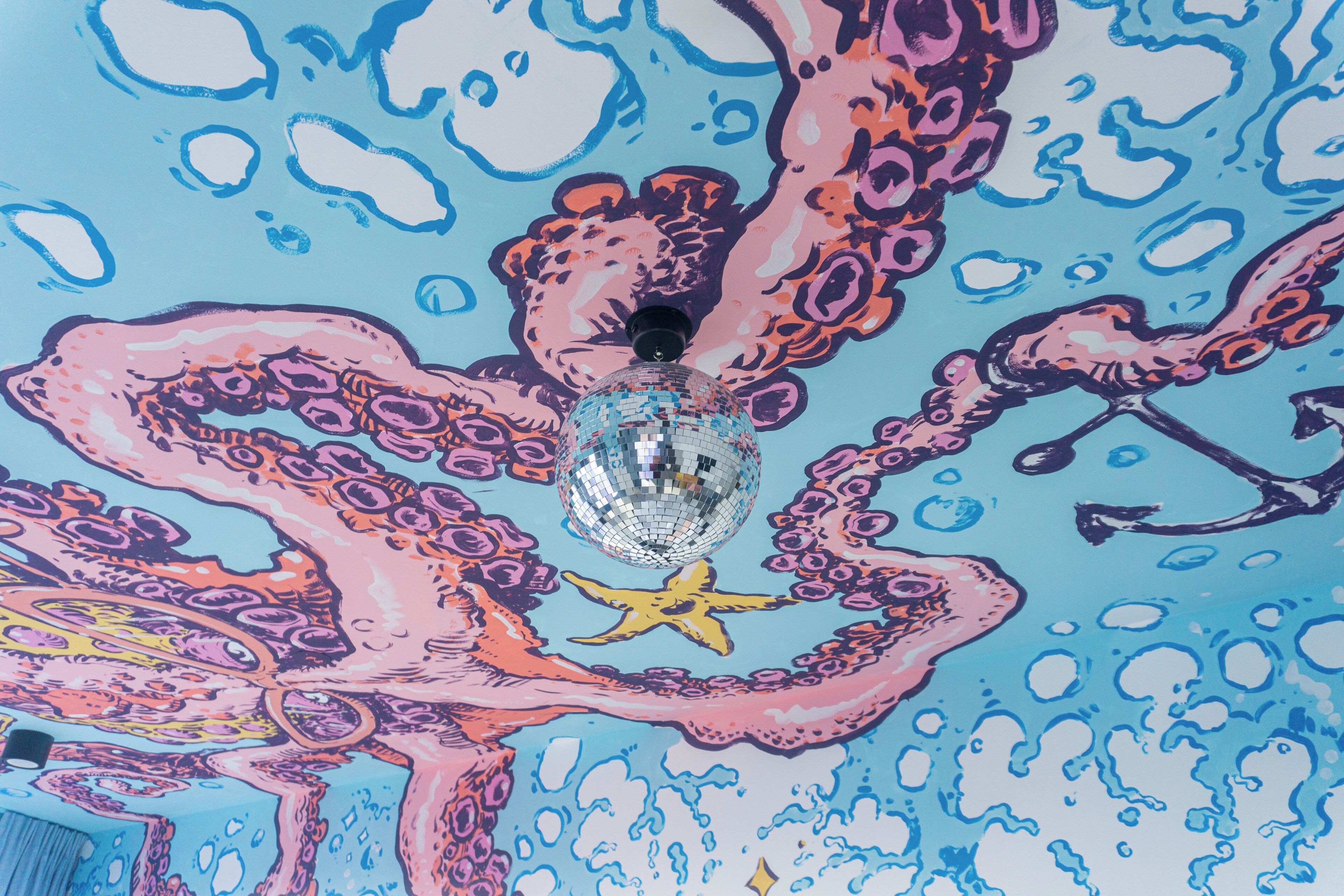 A ceiling with a vibrant octopus mural, a disco ball, and a starfish.