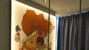 Habitació amb un mural gran a la paret que mostra un camió de dibuix animat, una armchair negra i una taula de fusta petita.