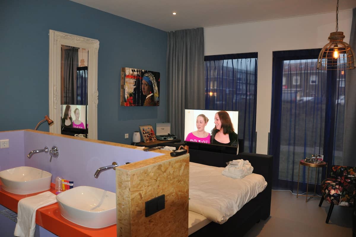 Hotellihuone, jossa on suuri kylpyamme, kaksi pesuallasta, sänky, televisio ja pieni pöytä.