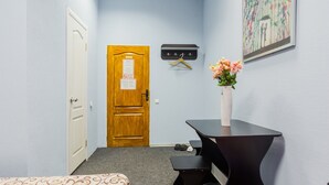A hallway with a wooden door, a coat rack, a small table, and a vase of flowers. - Guest House on Bessarabska Square (Kyiv)