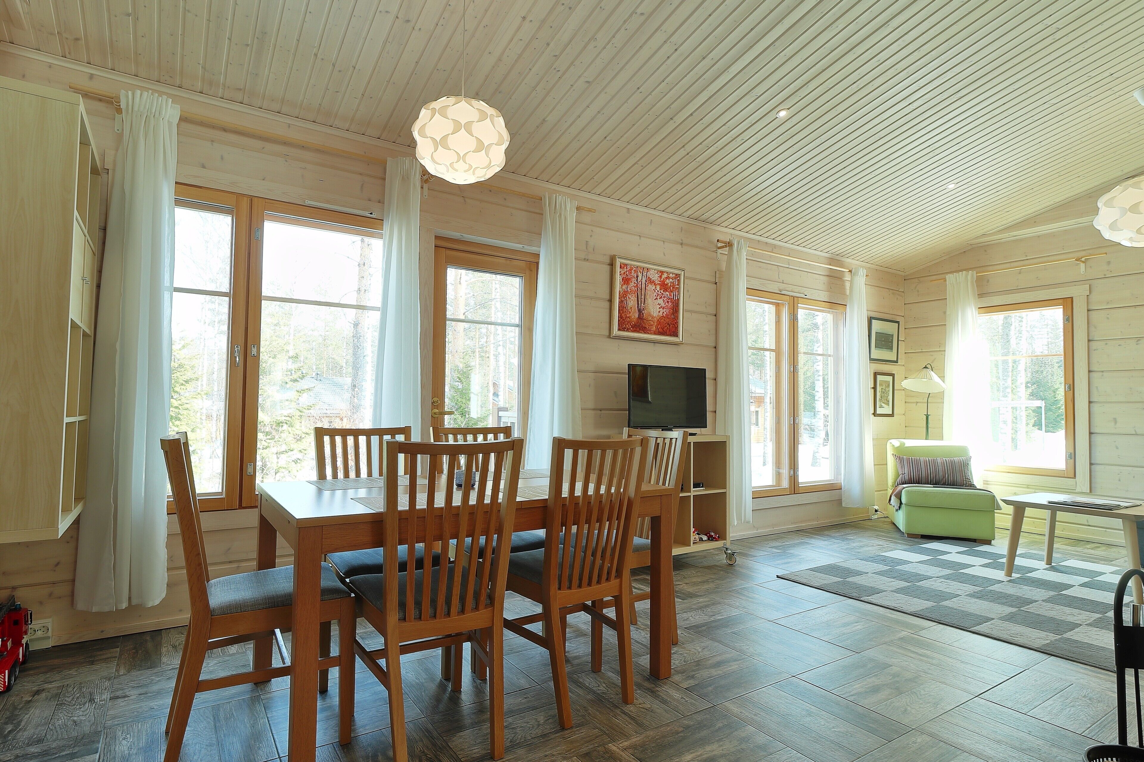 A spacious living area with a wooden dining table and chairs, a television, and a sofa.