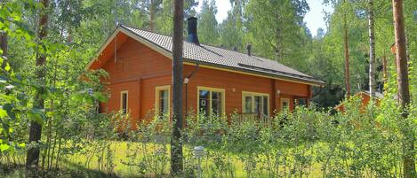 A wooden cabin with a sloped roof, surrounded by dense forest.