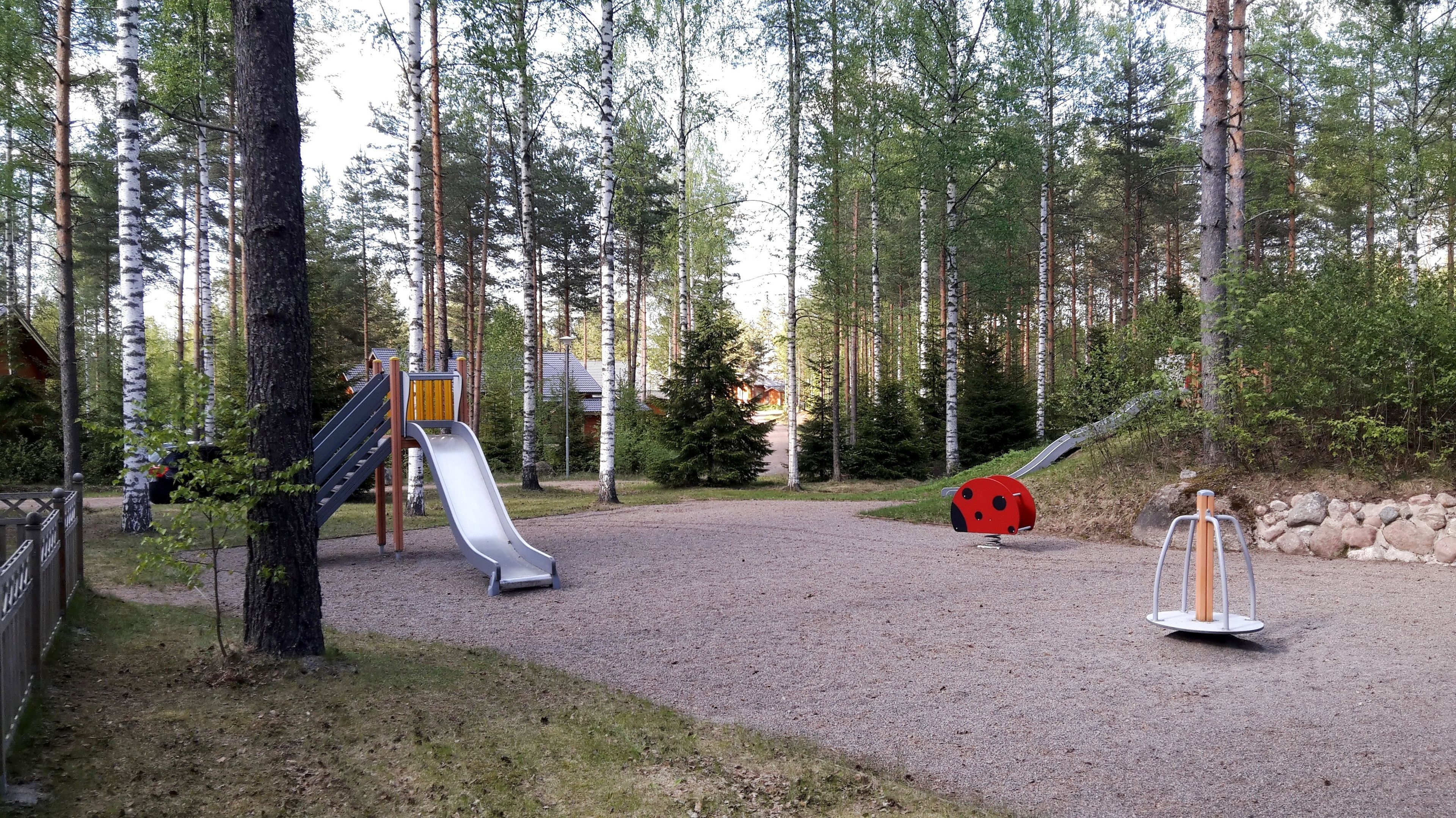 A playground with a slide and a red ladybug decoration in a forested area.